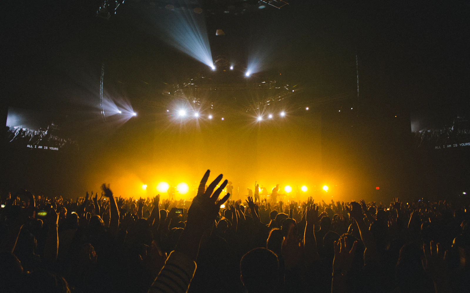 Público frente a un escenario iluminado con focos amarillos en un concierto