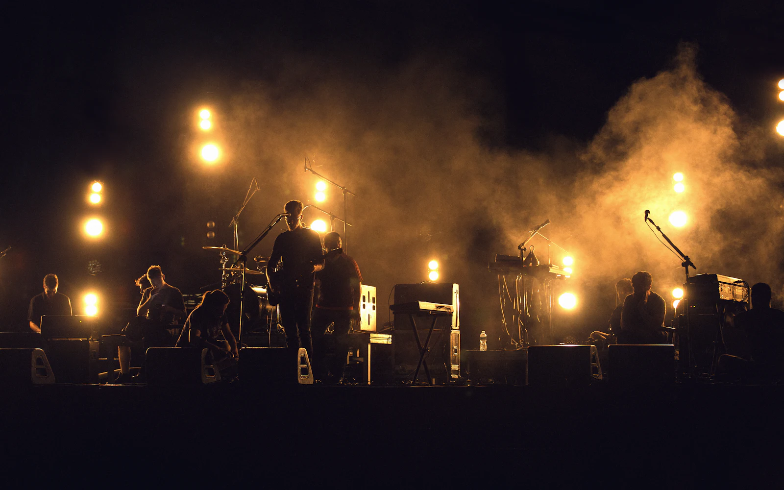 Banda en el escenario a contraluz con luces cálidas y humo