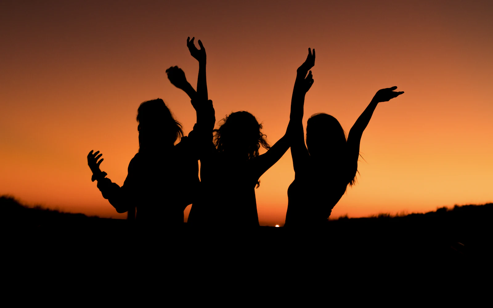 Siluetas de amigas bailando al atardecer