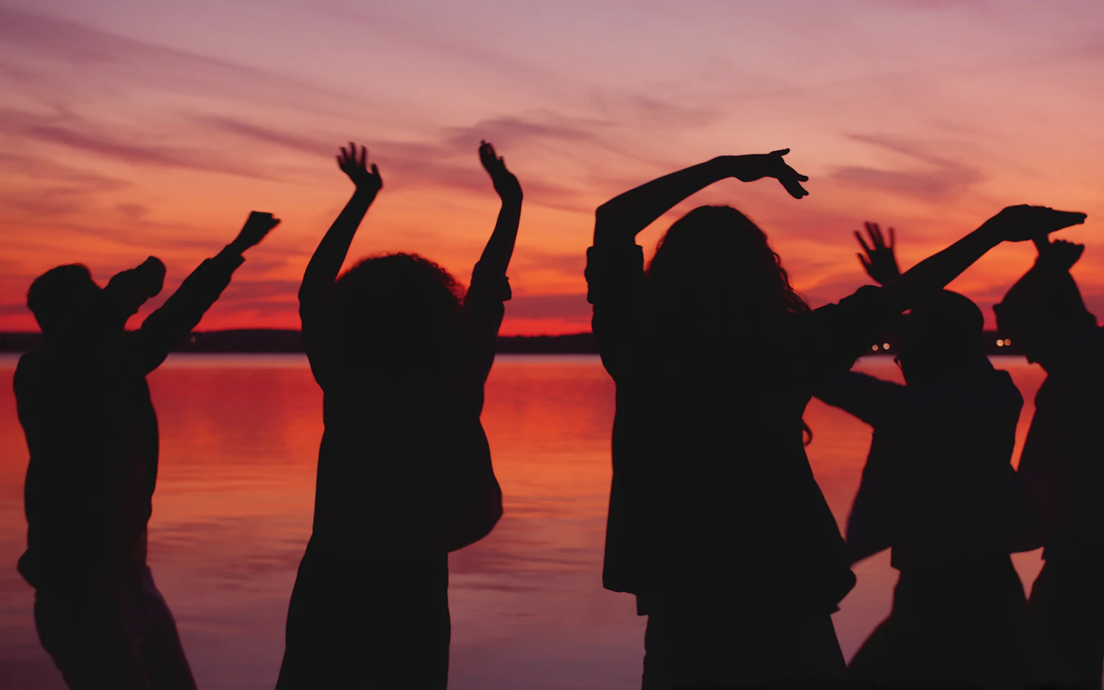 Siluetas de gente bailando al atardecer junto al agua