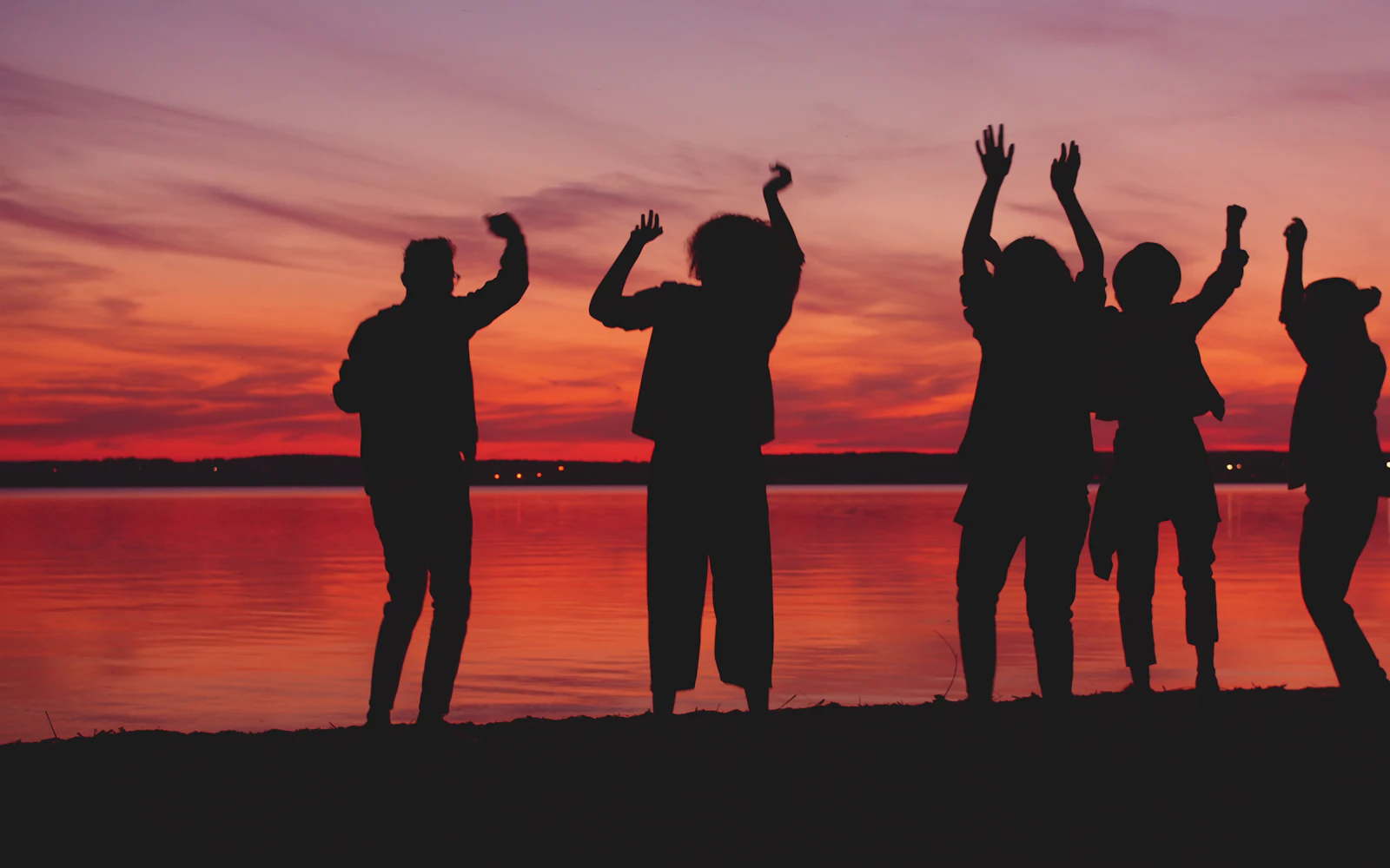 Amigos bailando al atardecer junto al agua